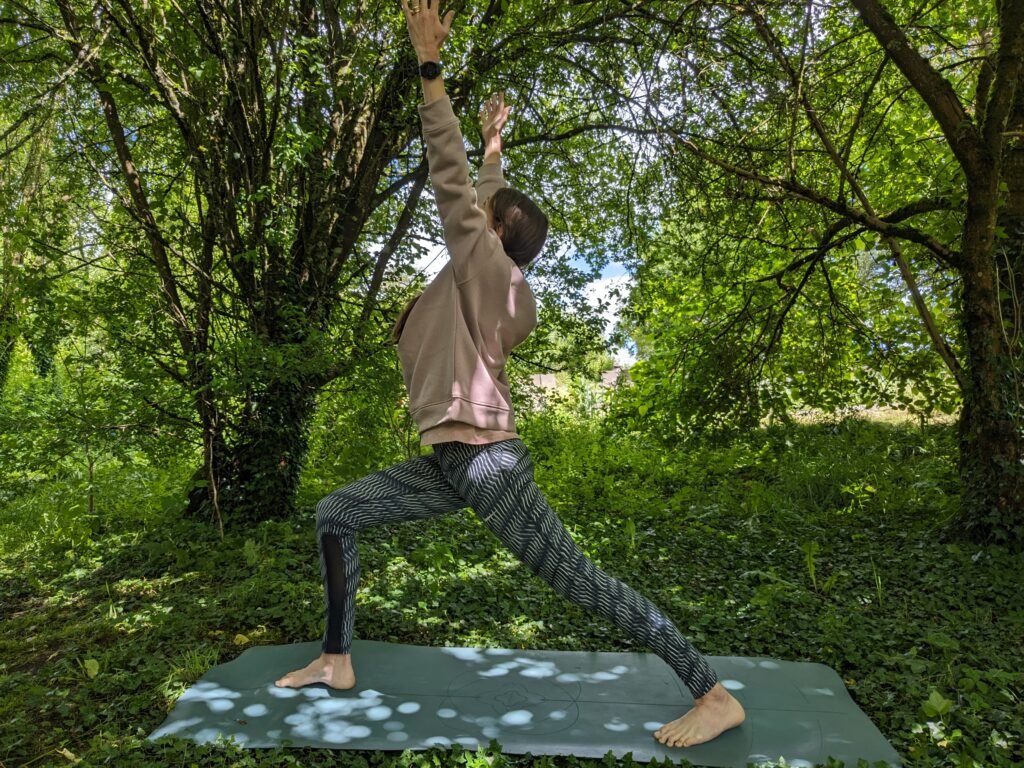Yoga teacher in warrior 1 outdoors, practicing hatha or vinyasa yoga in the garden under a tree — promoting balance and energy