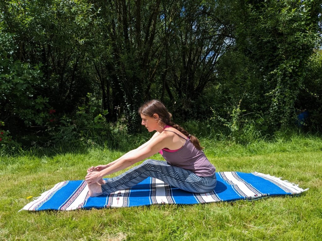 Yoga teacher practicing dandasana with knees bent in the garden, showing that yoga is adaptable and doesn't need physical flexibility.