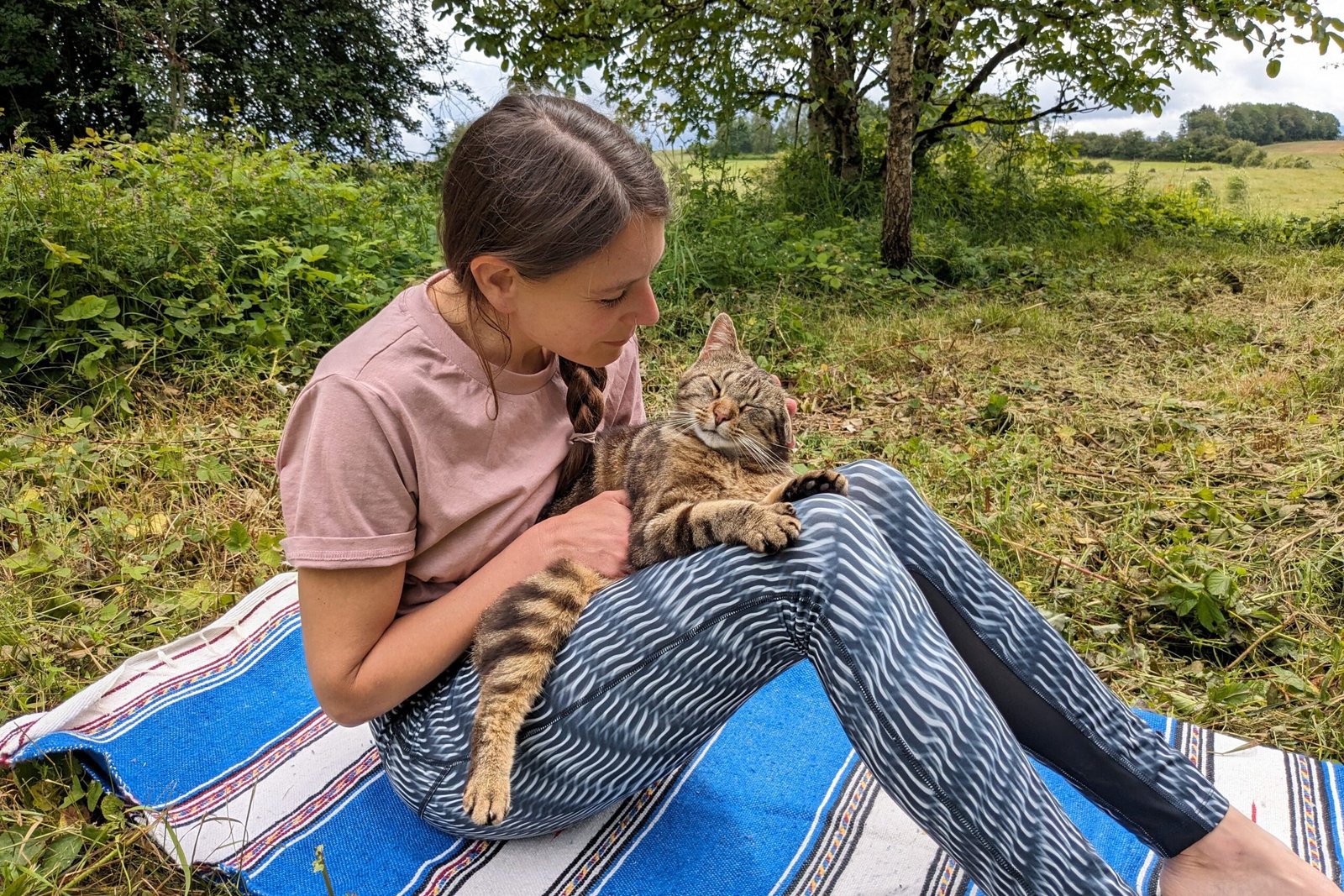 Yoga teacher seated outdoors looking at her cat in the garden — promoting taking time to be present